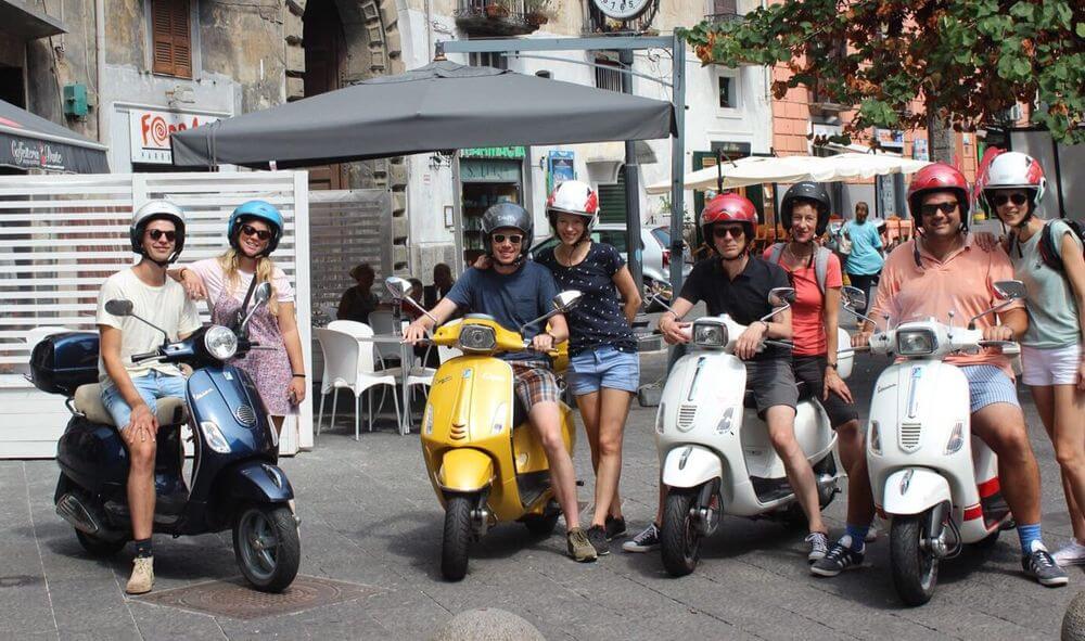 A group of tourists riding a vespa, on a vespa tour in Naples, Italy.